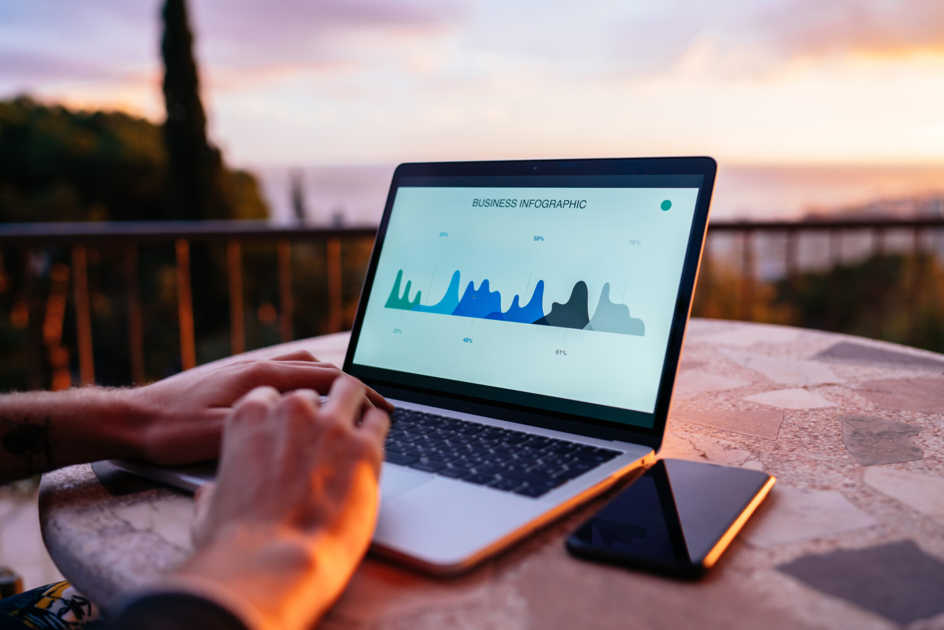 Crop male freelancer sitting at table on terrace in summer evening and browsing laptop while working on business project remotely