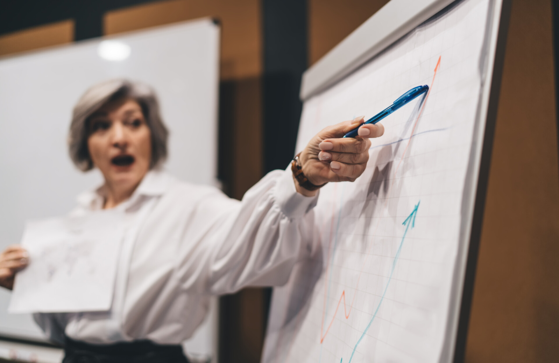 Pensive female pointing at sheet of paper on whiteboard and explaining details of new project while working in contemporary workplace