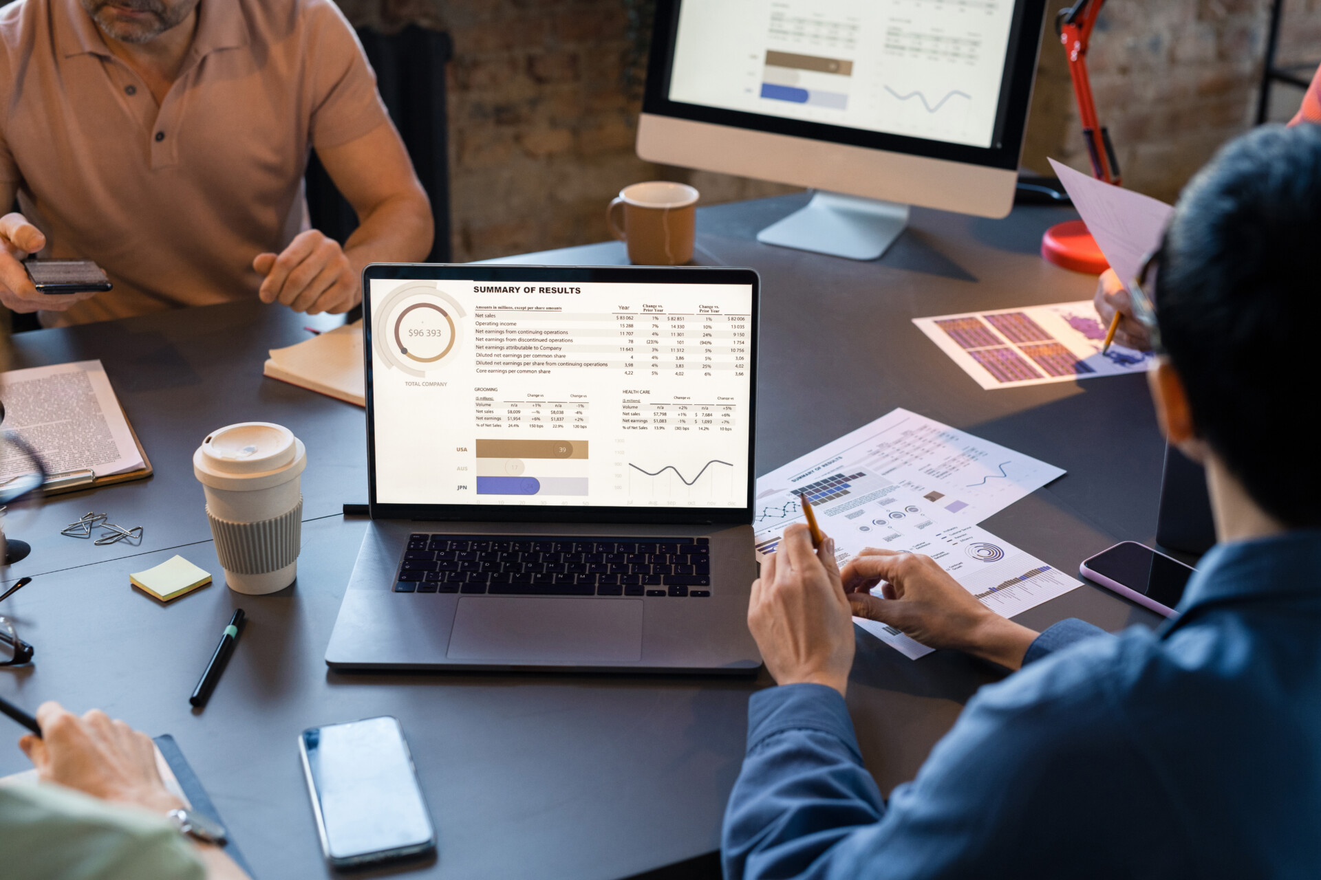 Close-up of business people sitting at the table with laptop and looking at monitor with financial grpahs during teamwork at meeting